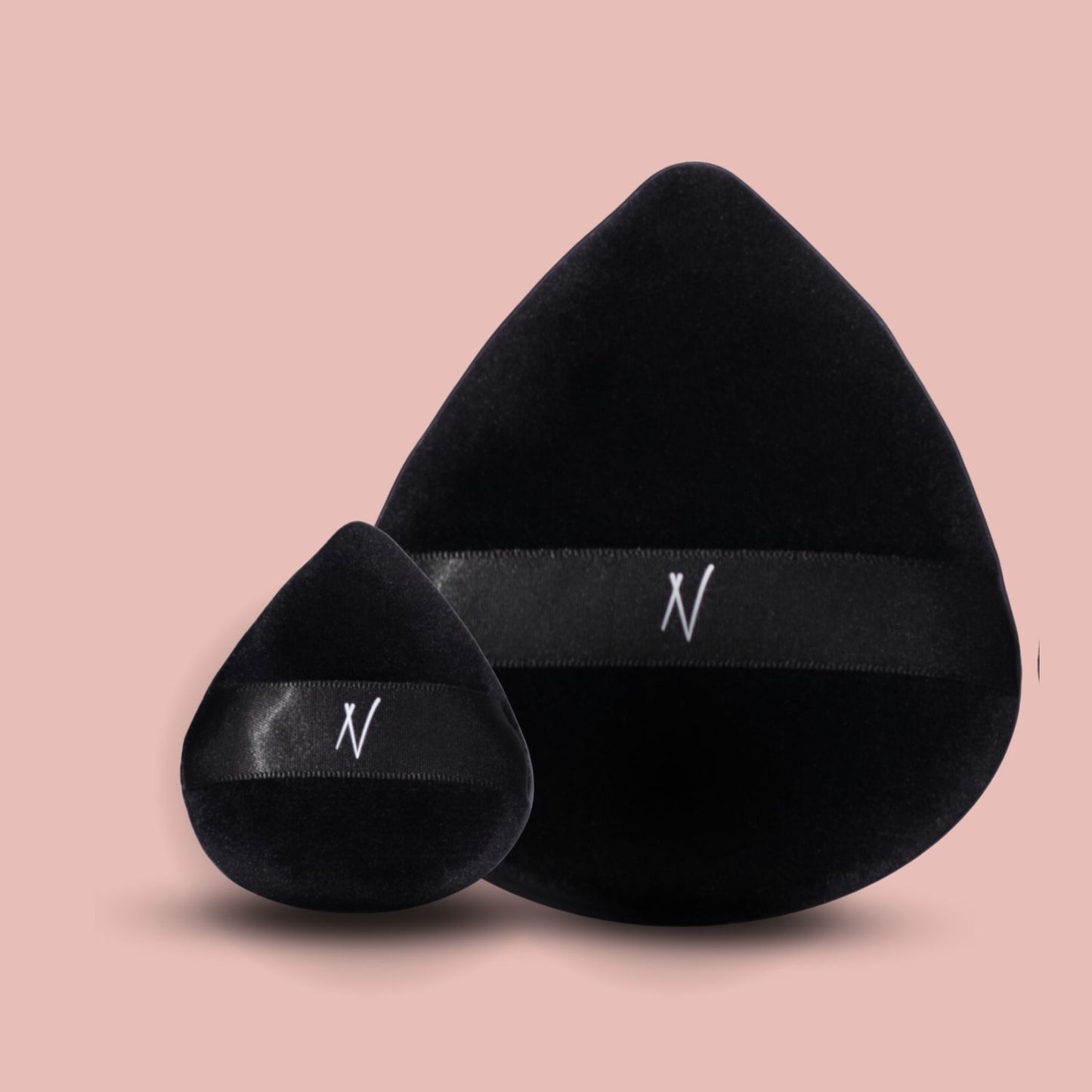 Two black velvet powder puffs, one large and one small, on a pink background.