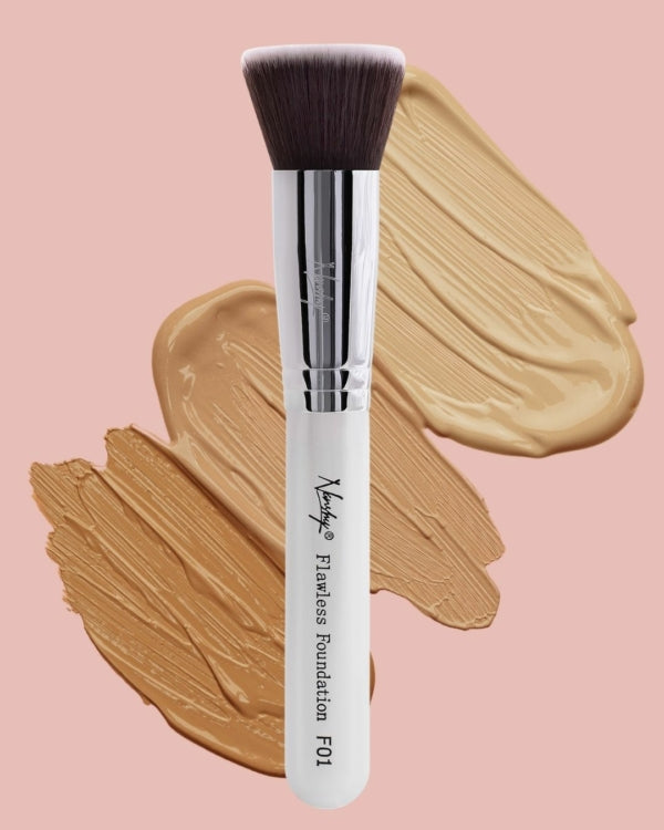Close-up of Nanshy Flawless Foundation Brush with soft, dense bristles and a sleek handle, surrounded by swatches of cream and powder foundation on a pink background.